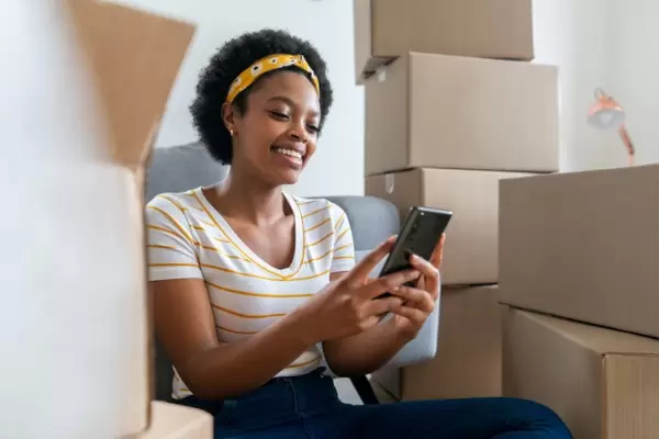 Woman looking at cell phone among moving boxes